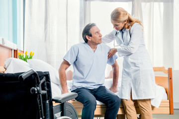 middle aged patient sitting on bed and doctor standing near him in hospital