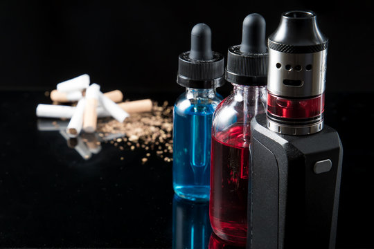 Pile of tobacco cigarettes and a vaporiser with 2 juice bottles