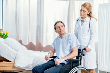 Obraz premium elderly man sitting in wheelchair and doctor standing near him in hospital
