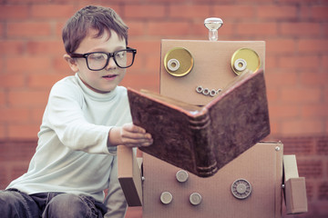 One little boy reading to  robot from cardboard boxes outdoors.