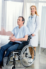 elderly man sitting in wheelchair and doctor standing near him in hospital