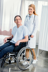 Obraz premium elderly man sitting in wheelchair and doctor standing near him in hospital