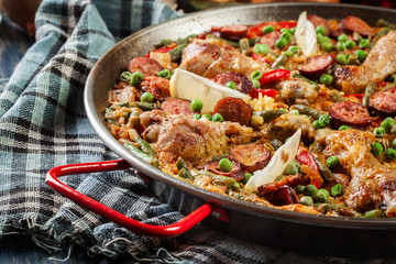 Traditional paella with chicken legs, sausage chorizo and vegetables served in paellera