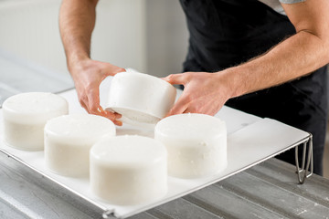 Close-up of a man forming cheese into the plastic molds at the small producing farm