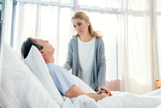 Side View Of Wife Visiting Upset Elderly Husband In Hospital