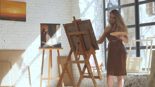 Artist paints picture on canvas with oil paints in workshop