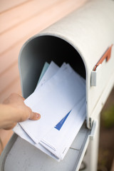 Letters in a mailbox are being held by a hand.