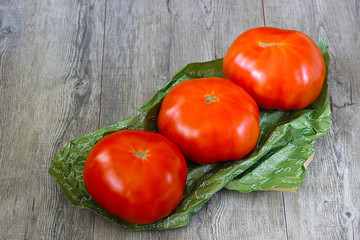 Ripe whole large tomatoes  on a green paper and a on gray wooden background.