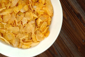 Tasty golden cornflakes in a white bowl on a wooden table. Top view flat lay