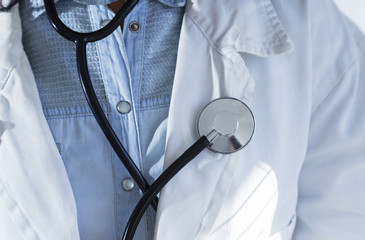 Medical doctor in white gown on white background holding a stethoscope. Focus on the stethoscope.