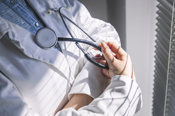 Medical doctor in white gown on white background holding a stethoscope. Focus on the stethoscope.