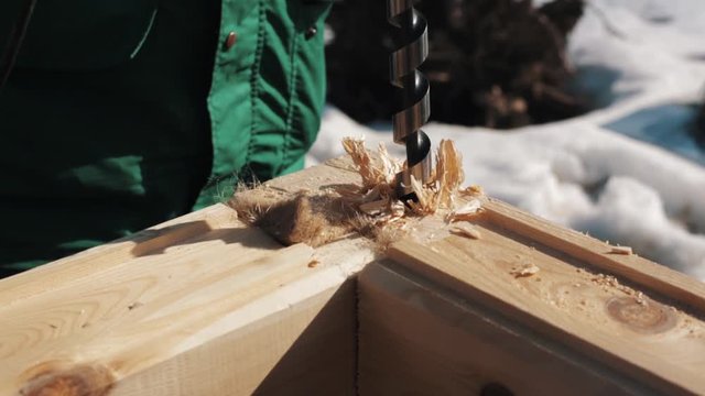 Close up boring hole in two wooden blocks corner connection creating sawdust outside in winter, snow on background
