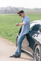 Junger Mann wartet bei seinem Auto und schaut auf die Uhr