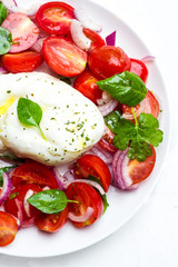Burrata with basil, tomato and red onion close-up on a white background.