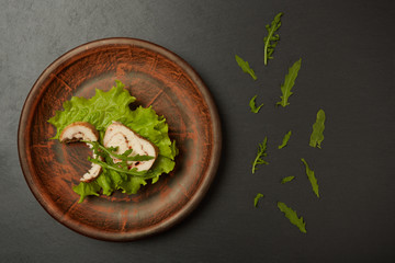 Healthy supper. Bitten sandwich with baked chicken breast with arugula and lettuce, on a clay plate. Top view.