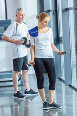 sportswoman and senior sportsman training with dumbbells in sports center