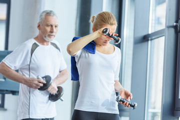 Obraz premium sportswoman and senior sportsman training with dumbbells in sports center