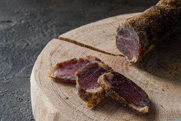 Slices of dried meat on wooden cut on dark rustic background. Snack and appetizer concept