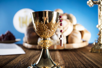 First Holy communion. Catholic theme. Crucifix, chalice, bible, bread on rustic wooden table and blue background.