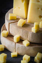 Close up of Swedish hard yellow cheese with holes chopped on wooden slices on dark rustic background