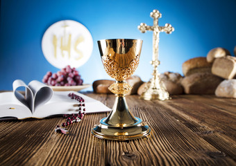 First Holy communion. Catholic theme. Crucifix, chalice, bible, bread on rustic wooden table and...