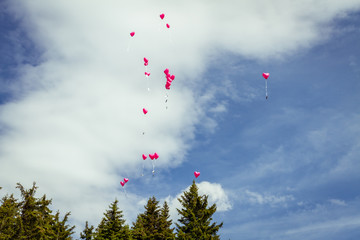 pink heart balloons flying in blue sky at wedding
