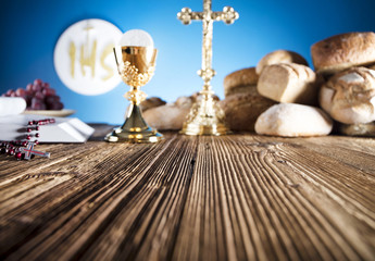 First Holy communion. Catholic theme. Crucifix, chalice, bible, bread on rustic wooden table and blue background.
