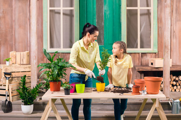 mother and daughter with plants and flowerpots standing at table on porch