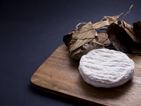 French banon cheese on wooden cutting board with its chestnut leaves, isolated on black background