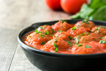 Meatballs with tomato sauce in iron frying pan on wooden table