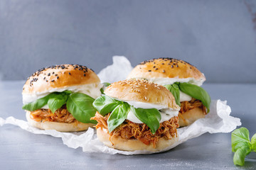 Homemade mini burgers with pulled chicken, basil, mozzarella cheese and yogurt sauce on baking paper over gray texture background. Healthy fast food concept
