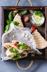 Pita bread sandwiches with grilled vegetables paprika, eggplant, tomato, basil and feta cheese served in wooden tray over gray stone background. Healthy fast food concept. Top view.