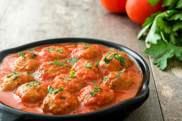 Meatballs with tomato sauce in iron frying pan on wooden table