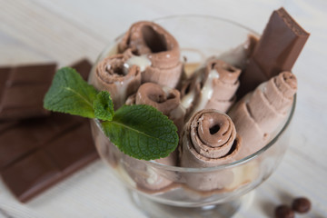 Roll of chocolate ice cream. Fresh fried ice cream, ice roll on a light wooden background. Ice cream with chocolate and mint