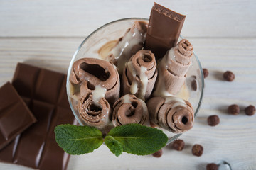 Roll of chocolate ice cream. Fresh fried ice cream, ice roll on a light wooden background. Ice cream with chocolate and mint