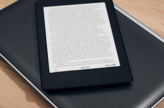 E-Reader With Blurred Text Over Closed Laptop On Wooden Background Closeup