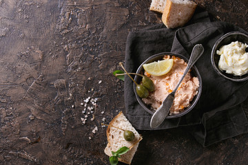 Black bowl of salmon pate with red caviar served with butter, sliced bread, capers, vintage knife...