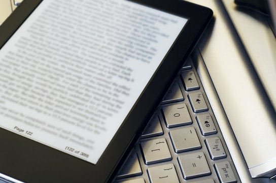 Closeup Of Electronic Book Reader With Blurred Text On Silver Laptop Keyboard 