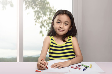 Happy asian child drawing with crayon on white paper