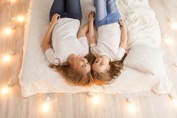 Mother and daughter lay on the bed and look at the camera. View from above. Togetherness. Loft interior