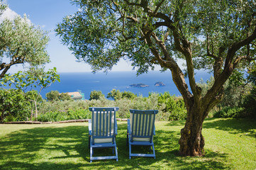 Holiday on Amalfi coast - two deck chairs under a tree, blue sea and Li Galli island view, Italy