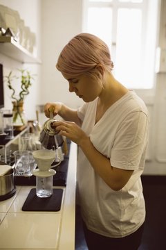 Female barista pouring hot water through funnel