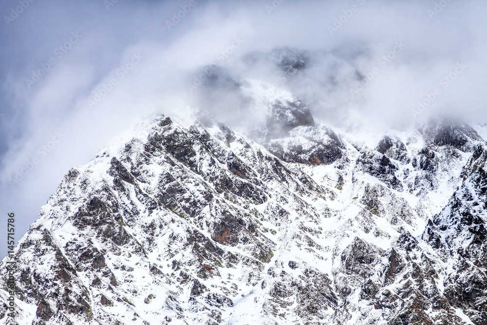 Wall mural Beautiful dramatic snowy mountain peaks in clouds. Scenic winter landscape