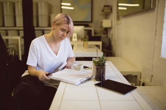 Female barista writing on clipboard while sitting