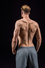 Fototapeta premium back view of shirtless bearded bodybuilder posing isolated on black in studio