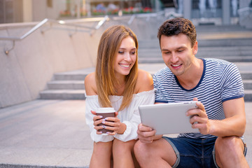 Romantic date. Pretty young loving couple using tablet computer together outdoor.