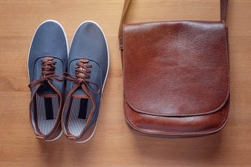 Outfit of traveler, student, teenager, young man. Overhead of essentials for modern young person. objects on wooden background  include gumshoes and leather bag.