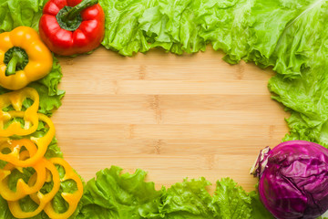 Copy space on a wooden or bamboo background, covered with vegetables, lettuce, red cabbage, red and yellow pepper. You can write here your menu or any inscription