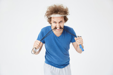 Aggressive man in bright sport outfit biting jumping rope