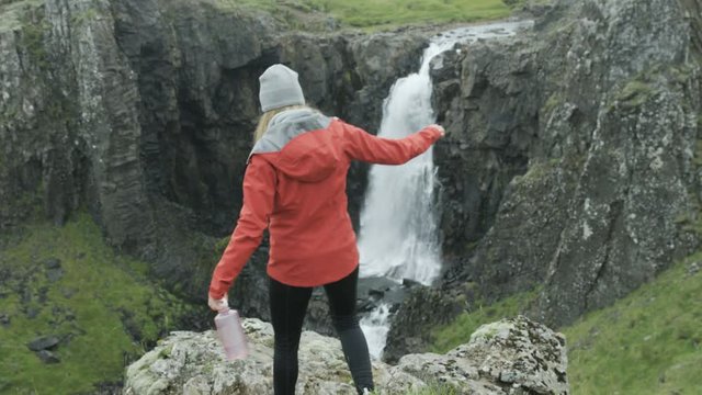 woamn walks towars cliff to check out view of waterfall in Iceland